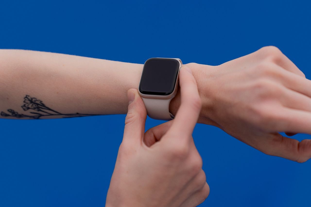 A person adjusting a modern smart watch against a bright blue background.