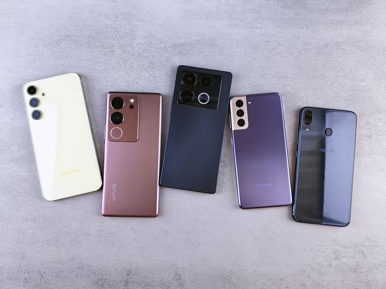 Flat lay of five modern smartphones on a gray surface, showcasing various designs.