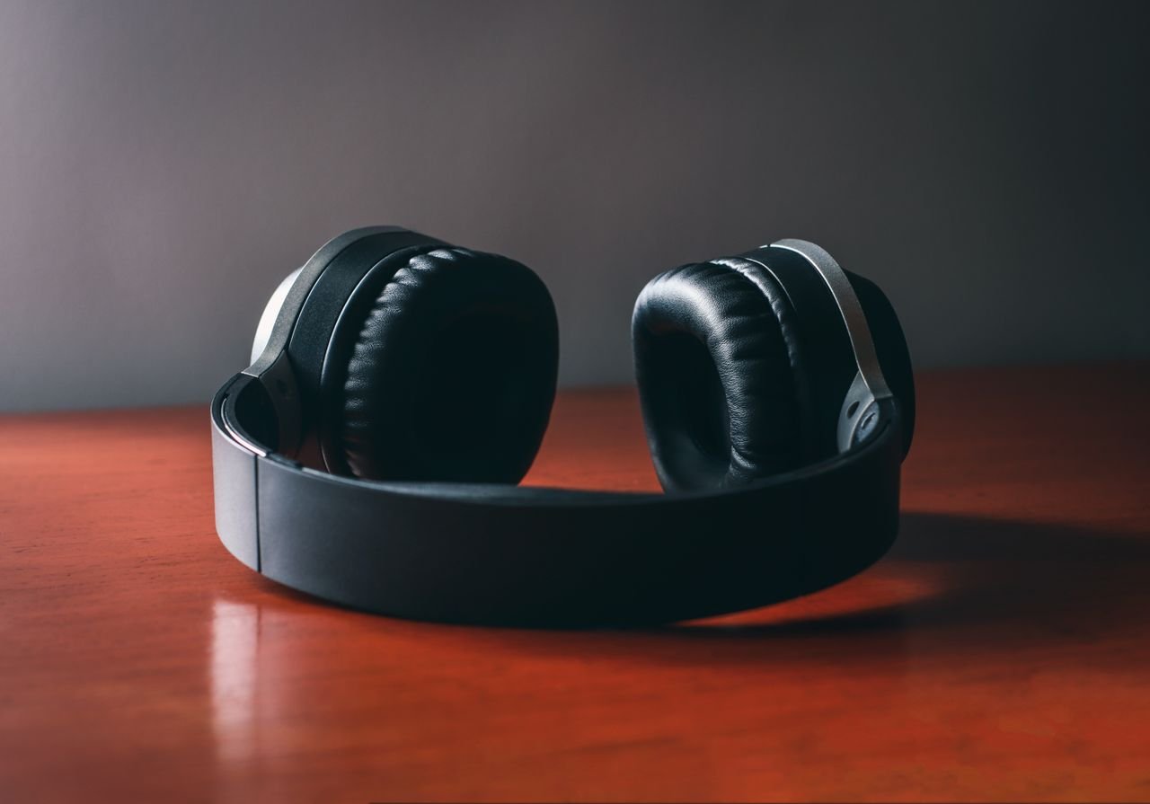 Close-up of sleek wireless headphones placed on a polished wooden surface under soft studio lighting.